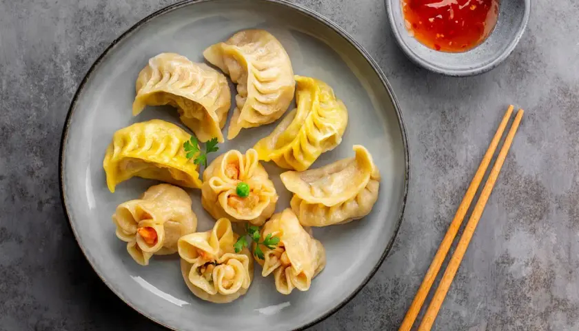 Talerz pełen różnorodnych pierożków dim sum, z sosem i pałeczkami. Idealna przekąska.
