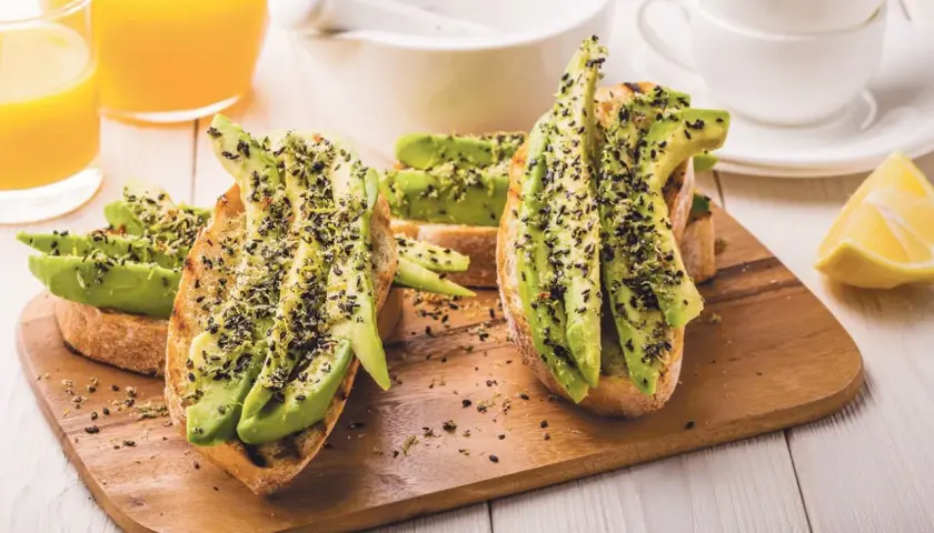 Tostadas con aguacate y semillas negras, perfectas para desayunos veganos. Acompañadas de zumo de naranja y limón.