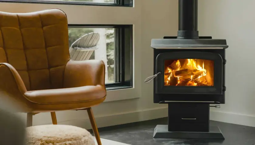Un confortable fauteuil en cuir brun fait face à un poêle à bois non étanche, où des flammes dansent joyeusement dans le foyer.