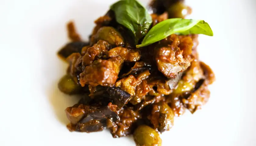 Un saporito piatto di caponata di pesce spada, con melanzane, olive e basilico fresco, pronto per essere gustato.