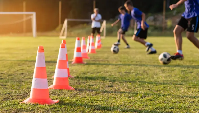 Trening piłkarski z użyciem pachołków, pokazujący jak uczyć futbolu. Dzieci ćwiczą drybling na boisku.