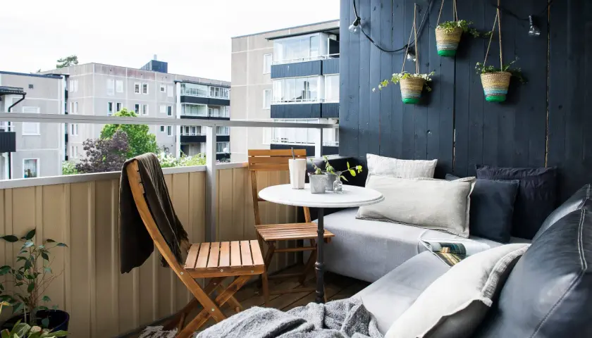 Mysig, inredd långsmal balkong med soffa, bord, stolar och hängande amplar. Perfekt för avkoppling.
