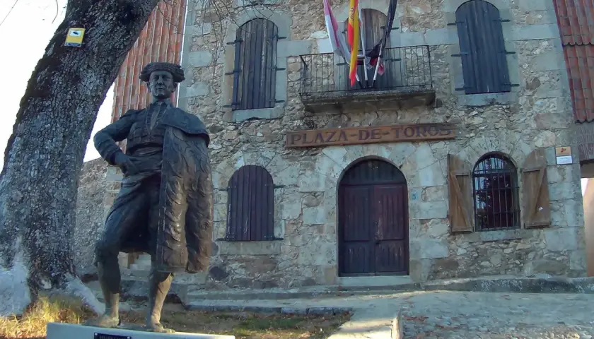Estatua de un torero frente a la plaza de toros la ancianita. El edificio de piedra tiene un letrero y banderas españolas.