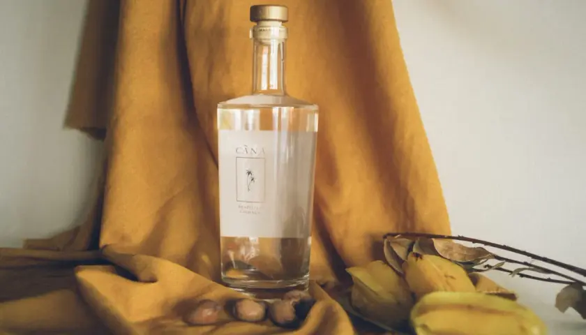 Butelka Cachaça Cãna, brazylijskiego alkoholu z trzciny cukrowej, otoczona owocami i suchymi liśćmi. Cachaca co to? To brazylijski skarb!