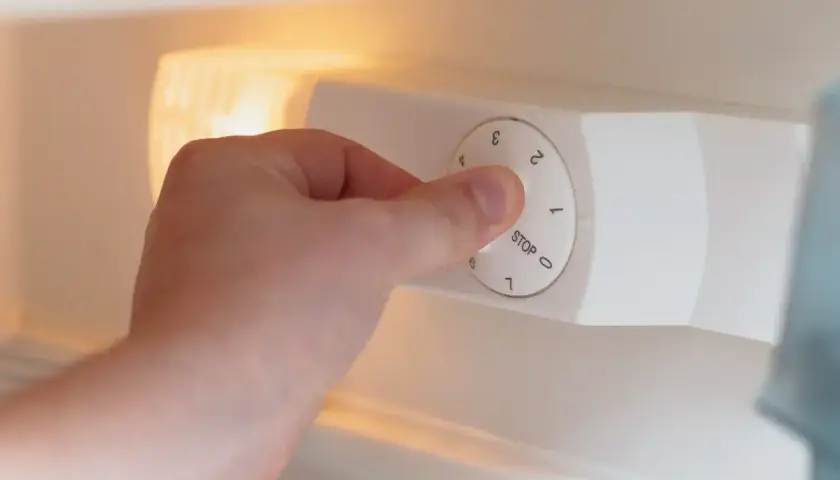 Dłoń kręci pokrętłem termostatu w lodówce, ustawiając temperaturę.