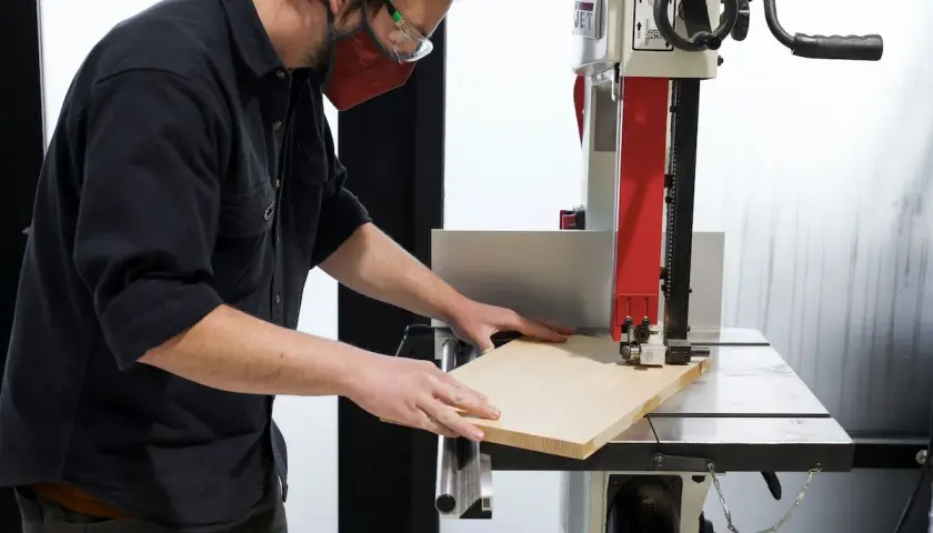Un artisan utilise une scie à ruban, un des outils pour couper le bois, pour façonner une planche.