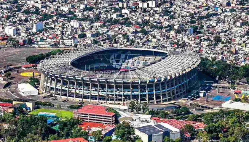 Widok z lotu ptaka na monumentalny stadion Azteca otoczony gęstą zabudową miejską.