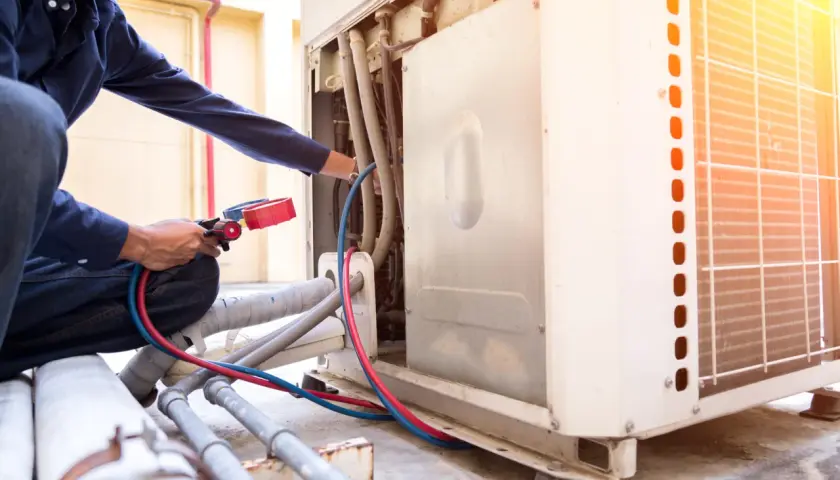 Técnico realiza soldadura con nitrógeno en unidad de aire acondicionado exterior, conectando manómetros a tuberías.
