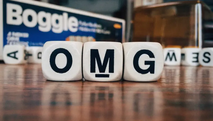 Dadi con lettere formano l'acronimo in inglese "OMG". Sullo sfondo, la scatola del gioco Boggle.