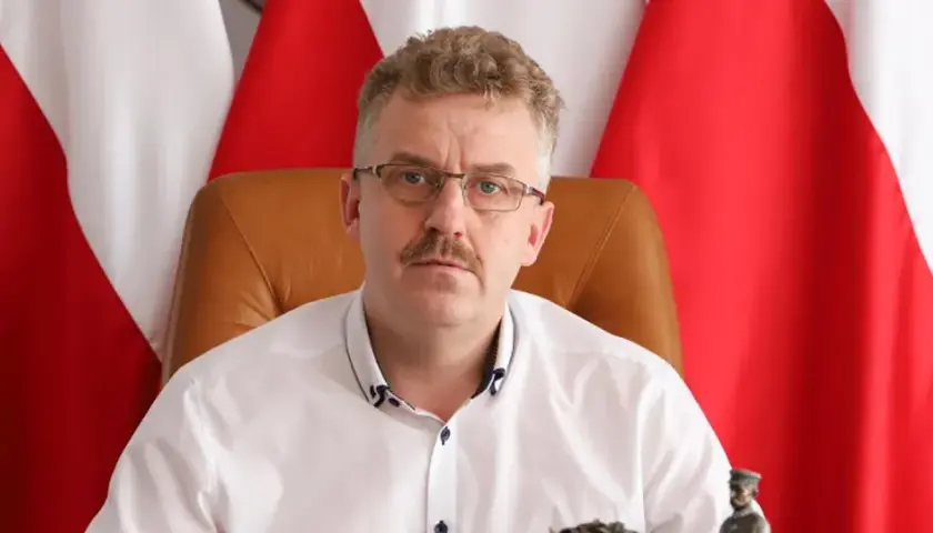 Starosta w okularach i białej koszuli, siedzący przed polskimi flagami, wygląda jakby właśnie skończył wykład o tym, co robi starosta na studiach.