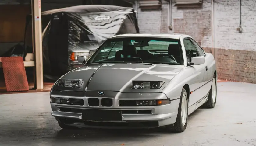 Un elegante BMW E31 plateado, un clásico deportivo, descansa en un garaje con paredes de ladrillo.