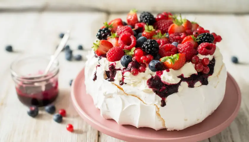 Beza pavlova która zawsze wychodzi, udekorowana bitą śmietaną i mnóstwem świeżych owoców leśnych.