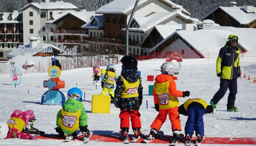 Dzieci na stoku, gotowe na ferie 2026. Wesołe kolorowe stroje narciarskie i śnieg wokół.