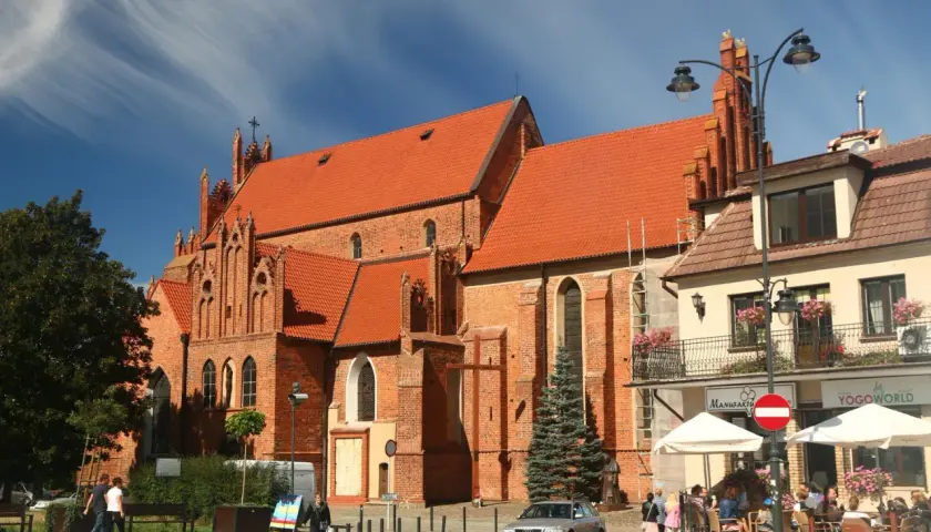 Starogard Gdański atrakcje: ceglana bazylika z czerwonym dachem i gotyckimi detalami, plac z kawiarnią i ludźmi.