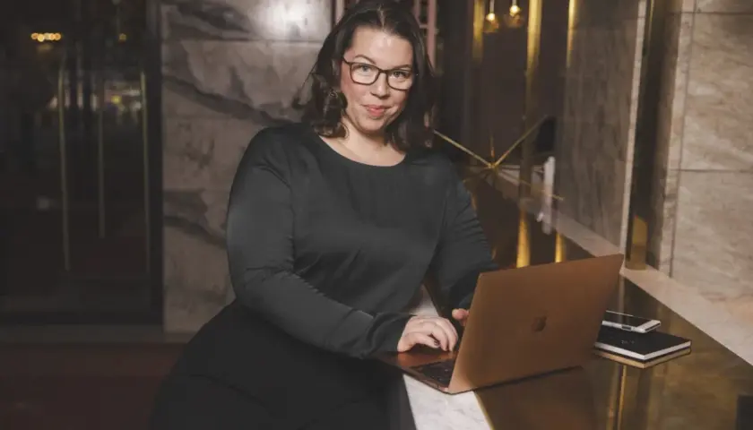 Linnea Molander, med glasögon och svart klänning, arbetar vid en bärbar dator i en lyxig miljö.