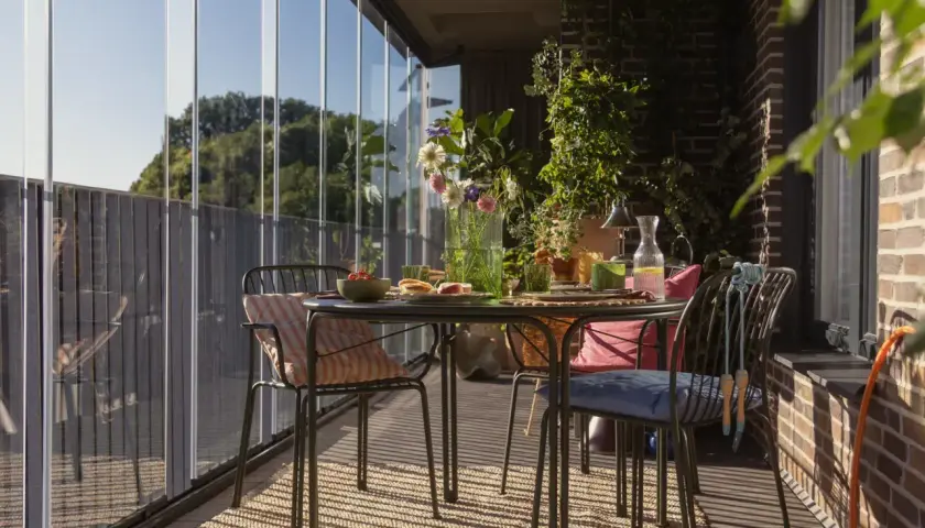 Jak zrobić balkon w bloku? Przytulny, przeszklony balkon ze stolikiem, krzesłami i mnóstwem zieleni. Idealne miejsce na poranną kawę.