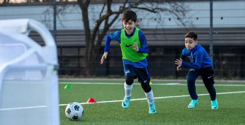 Zwei Jungen in Fußballtrikots trainieren auf einem Kunstrasenplatz. Sie sind voller Energie und Freude, während sie über das Feld rennen. Diese fussball spiele kinder sind ein toller Anblick!