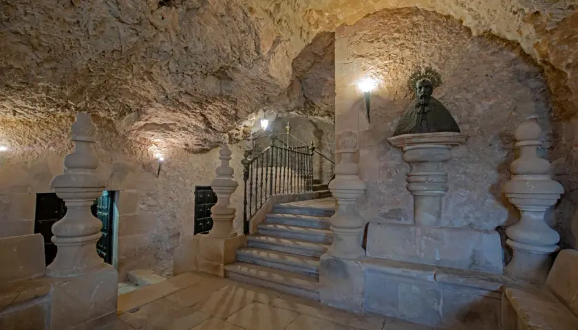 Busto de San Saturio en Soria, junto a escaleras de piedra y rejas, en un entorno rocoso.