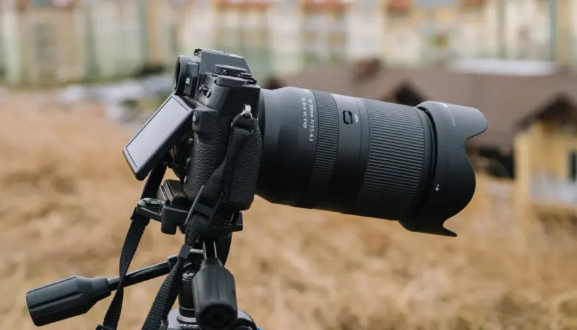 Aparat fotograficzny z obiektywem 18-300mm na statywie, z rozmytym budynkiem w tle.