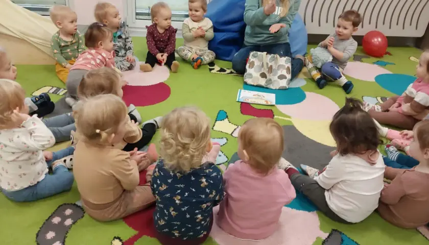 Nauczycielka pokazuje dzieciom w żłobku obrazki, inspirując angielski w żłobku pomysły. Dzieci siedzą na kolorowym dywanie.