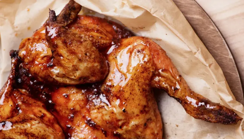 Pollo alla diavola succulento e dorato, con pelle croccante e lucida, servito su carta da forno.