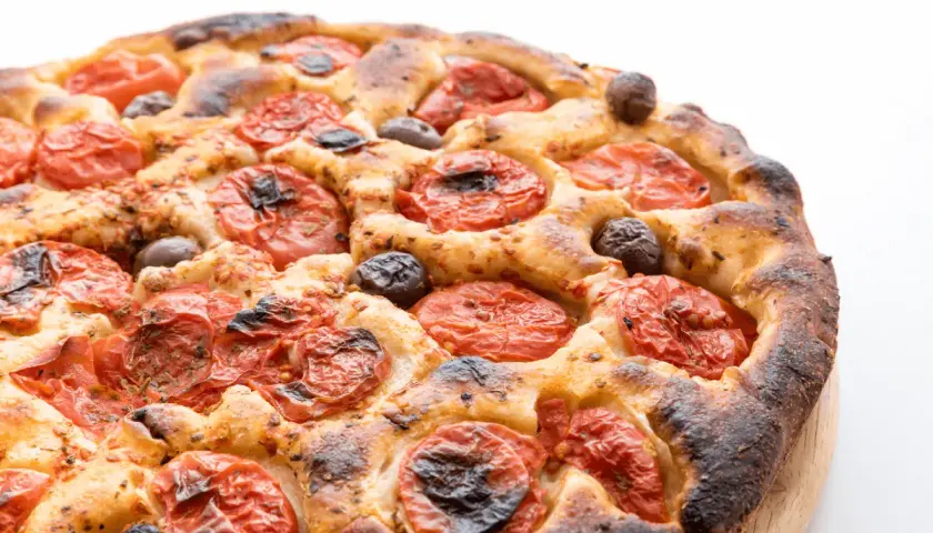 Focaccia barese dorata e fragrante, con pomodorini succosi e olive nere, pronta per essere gustata.
