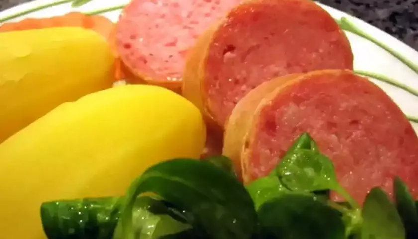 Tranches de saucisson savoureux accompagnées de pommes de terre jaunes et d'une salade verte fraîche.