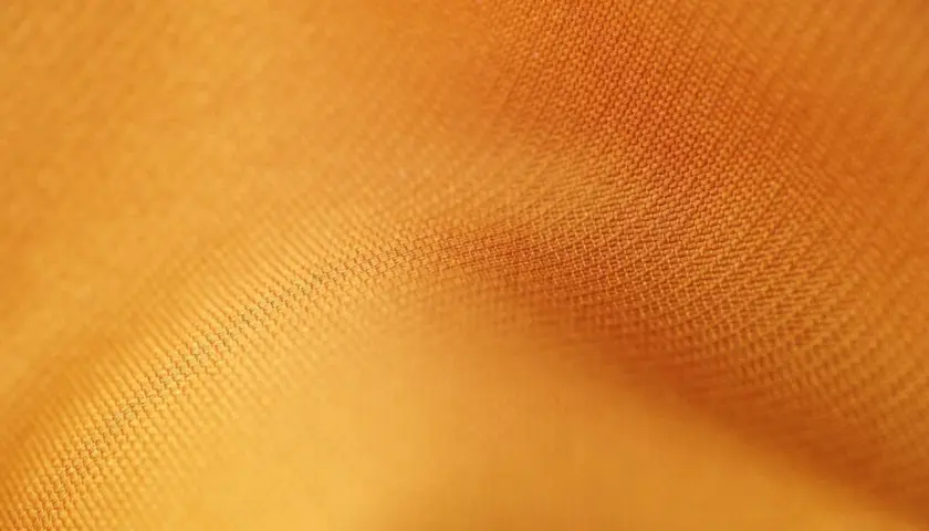 Texture d'un tissu orange vif, où chaque rayon fibre est visible, créant un motif subtil et doux.
