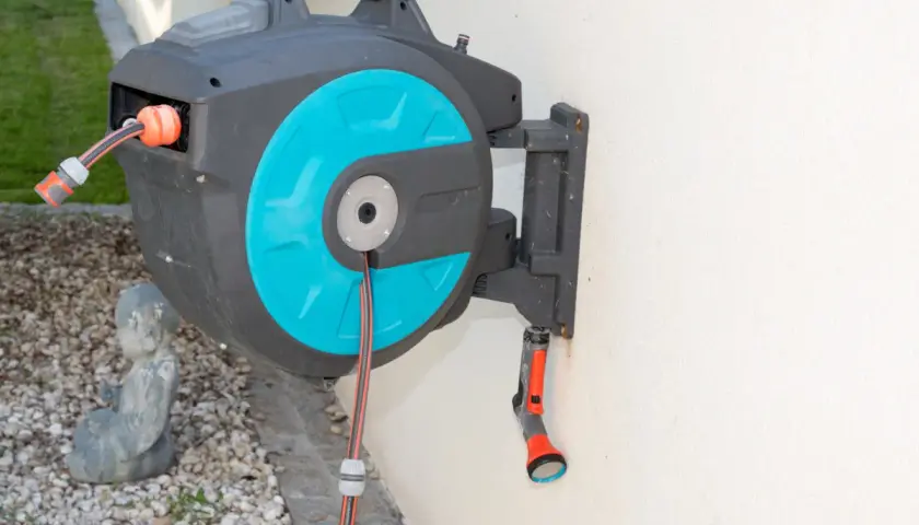 Ein schwarzer wandschlauchaufroller mit türkisfarbenen Akzenten hängt an einer weißen Wand. Ein Gartenschlauch ist teilweise aufgerollt.