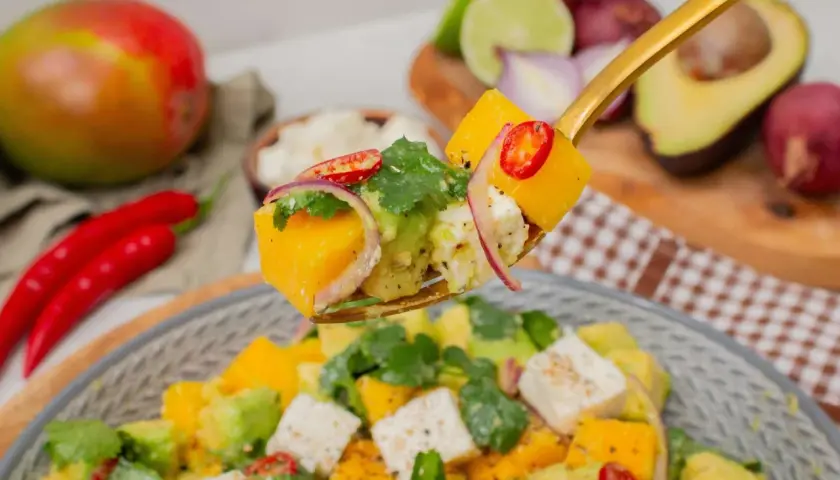 Ein Löffel voller Mango-Salat mit Avocado, Feta, roten Zwiebeln und Chili.