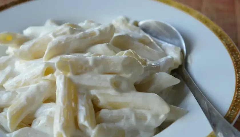 Makaron penne w kremowym sosie z twarogu na talerzu ze srebrną łyżką.