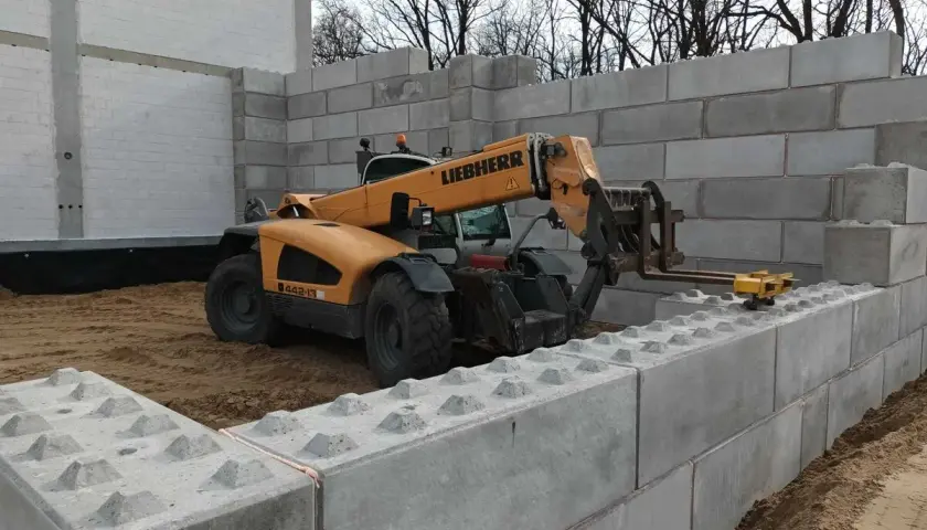 Żuraw budowlany stawia betonowe bloki, tworząc mur oporowy. Potrzebne jest pozwolenie na budowę.