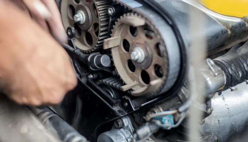 Meccanico lavora sul motore, sostituendo la cinghia di distribuzione. Il costo di questa operazione è importante per la manutenzione.