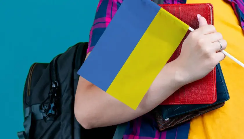 Osoba z plecakiem trzyma flagę Ukrainy i książki. Ceny we Lwowie mogą być różne, ale wiedza jest bezcenna.