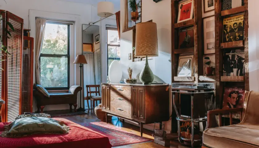 A cozy living room with vintage wood furniture styles, featuring a mid-century dresser, a wooden shelf unit displaying records, and a comfortable armchair.