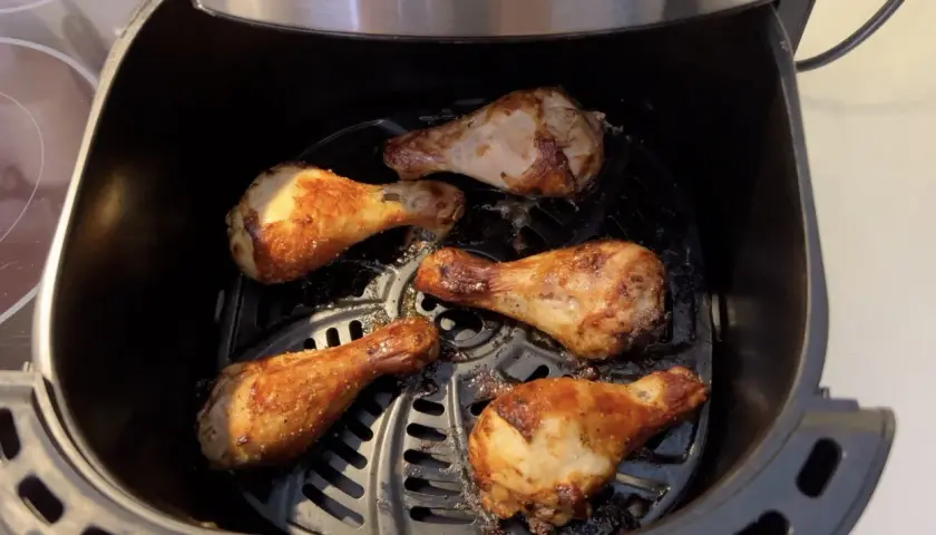 Cinq pilons de poulet dorés et croustillants cuisent dans une friteuse à air.