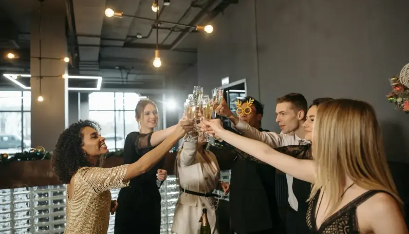 Grupa ludzi w eleganckich strojach na uroczystą kolację firmową wznosi toasty szampanem.
