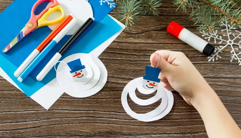 Niño crea muñecos de nieve con manualidades de invierno. Tijeras, rotuladores y pegamento listos para la diversión.