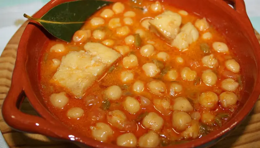 Garbanzos con bacalao, la receta de la abuela, servidos en cazuela de barro con hoja de laurel.