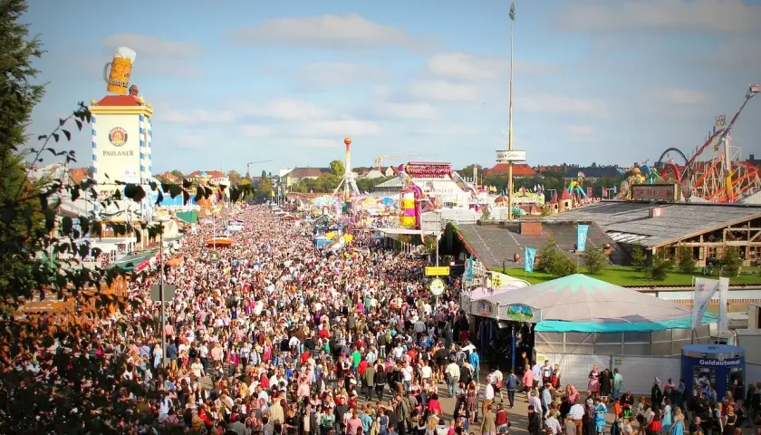 Tłum ludzi na festynie, widoczny wieżowiec z wielkim kuflem piwa i karuzele. To prawdziwy Oktoberfest!