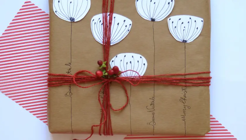 Confezioni pacchi regalo creativi con fiori stilizzati e bacche rosse, legati con spago rosso. Scritte "Buon Natale" e "Merry Christmas".