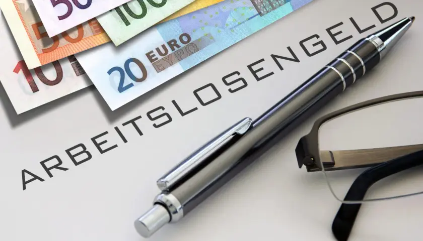 Euro-Scheine liegen neben einem Stift und einer Brille auf einem Dokument mit der Aufschrift "ABFINDUNG ARBEITSLOSENGELD".