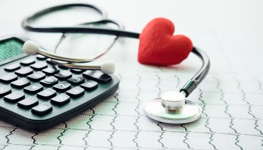 Kalkulator, stetoskop i czerwone serce na tle EKG symbolizują troskę o zdrowie i dobrowolne ubezpieczenie chorobowe.