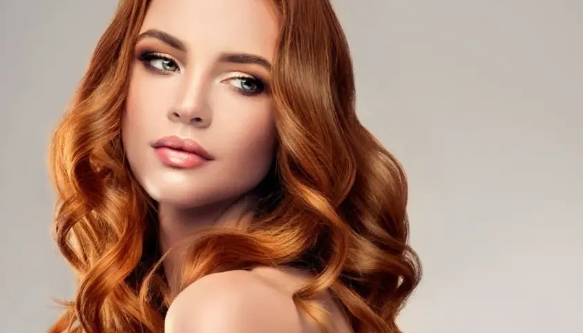 Miedziany blond dla kogo? Dla kobiety z falowanymi włosami i subtelnym makijażem, która emanuje elegancją i pewnością siebie.