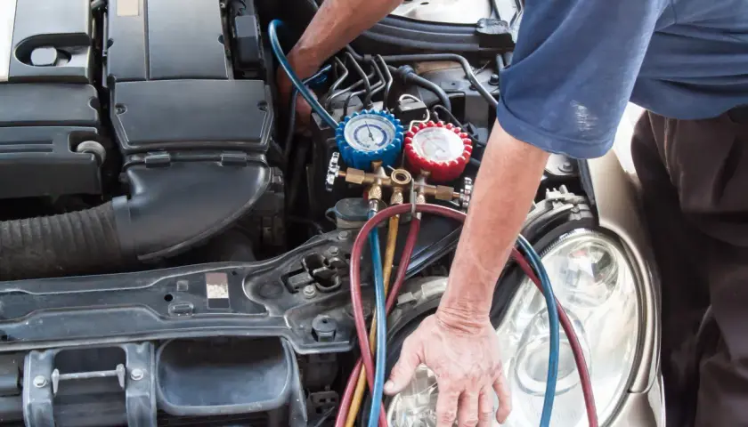 Mecánico realizando la tarea de cargar gas aire acondicionado en un coche, con manómetros y mangueras conectadas al motor.