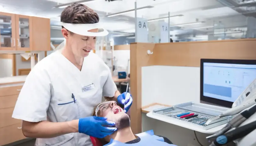 En tandhygienist i skyddsutrustning utför en undersökning på en patient. Detta är en del av en tandhygienist utbildning.