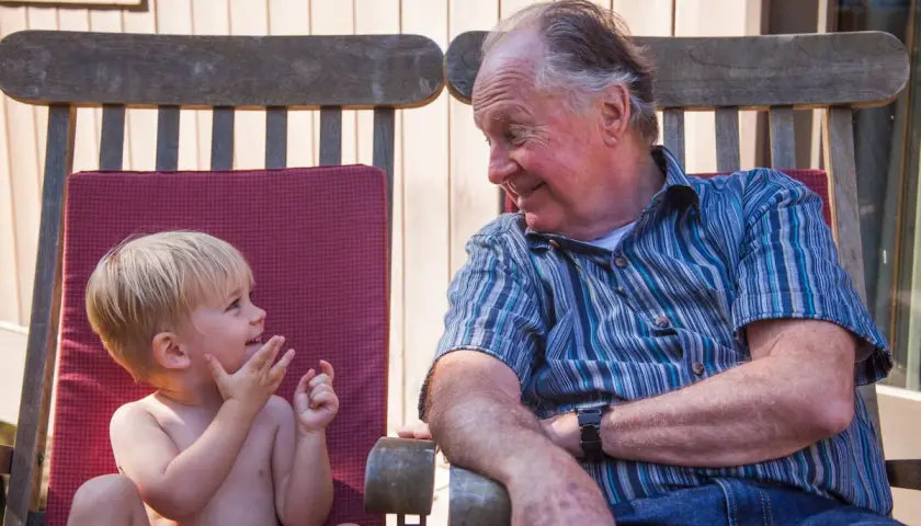 Un abuelo sonríe a su nieto, un momento tierno que los padres disfrutan al dejar a sus hijos con los abuelos.