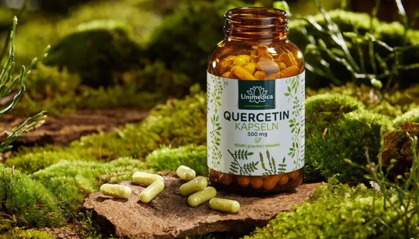 Flasche Quercetin-Kapseln neben einigen Kapseln auf Moos. Die Quercetin Wirkung auf die Psyche wird oft diskutiert.