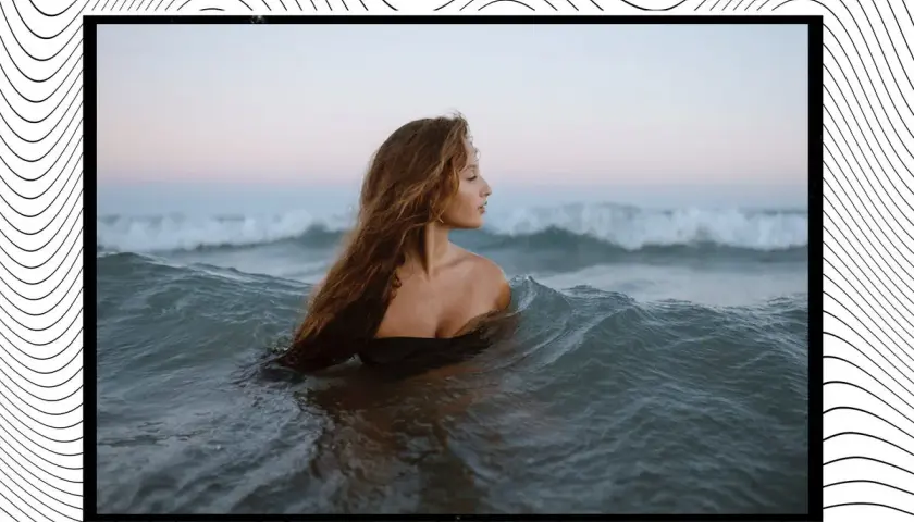 Mujer con cabello largo y ondulado se sumerge en el mar, rodeada de olas que parecen invitar a soñar con olas gigantes.