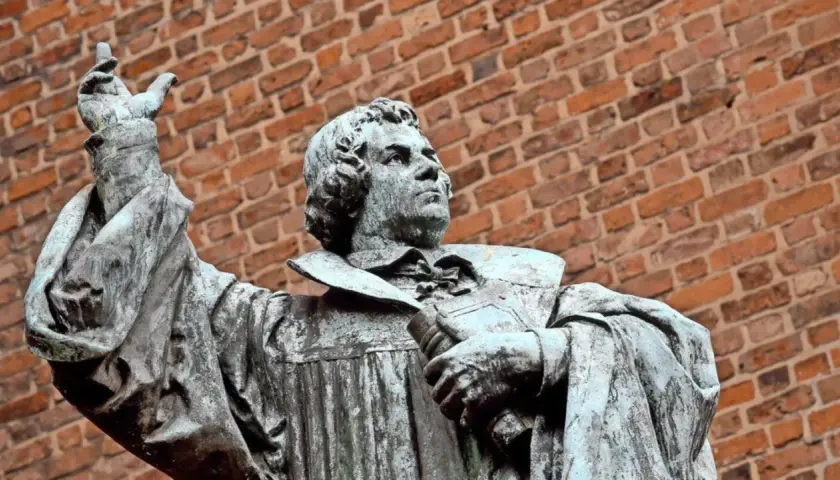 Statue eines Mannes mit Buch und erhobener Hand vor Ziegelwand. Ein Denkmal, das an den Reformationstag in Schleswig-Holstein erinnert.